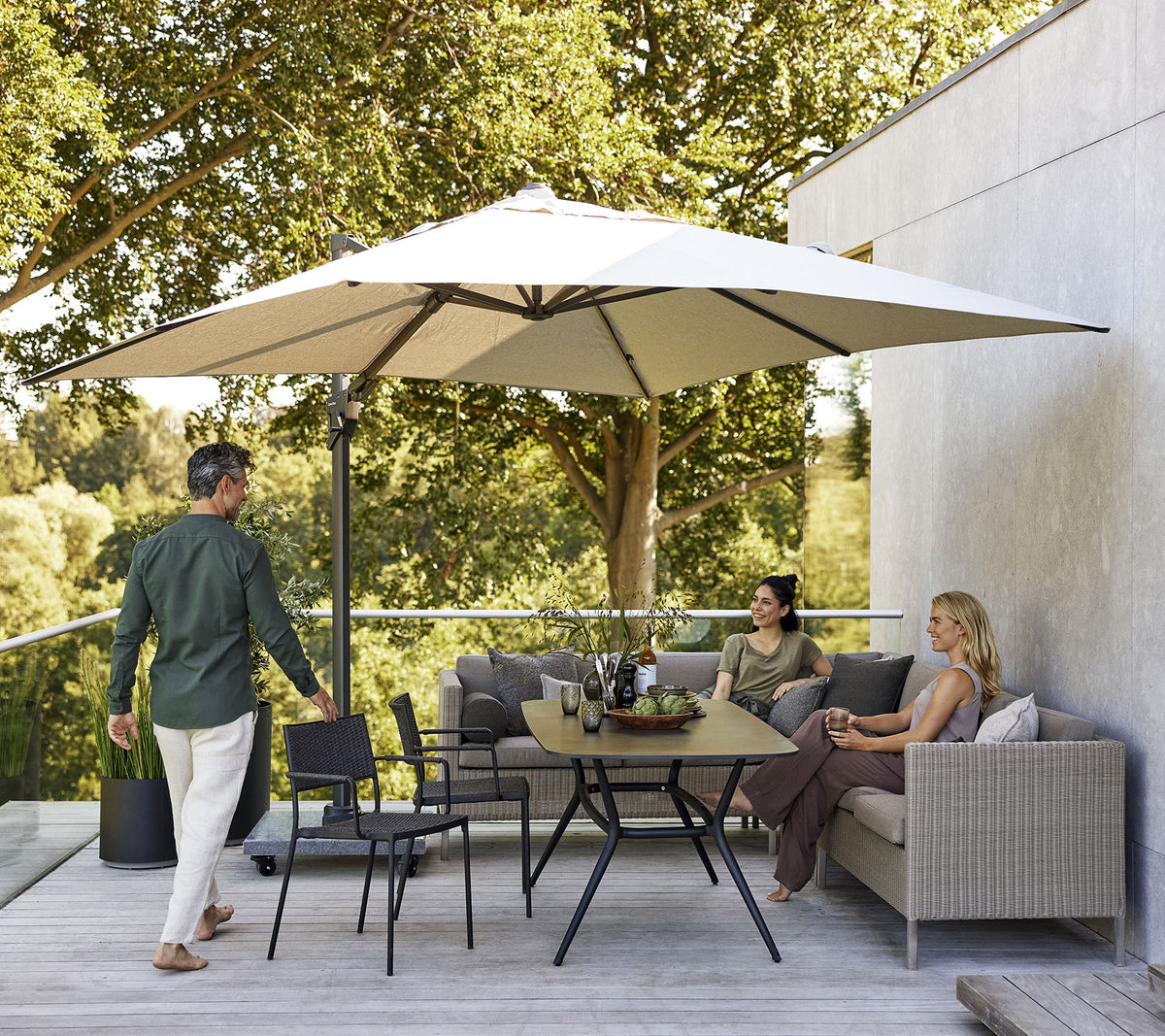 A stylish seating area with a large umbrella, featuring a sofa, chairs, and a dining table surrounded by lush greenery.